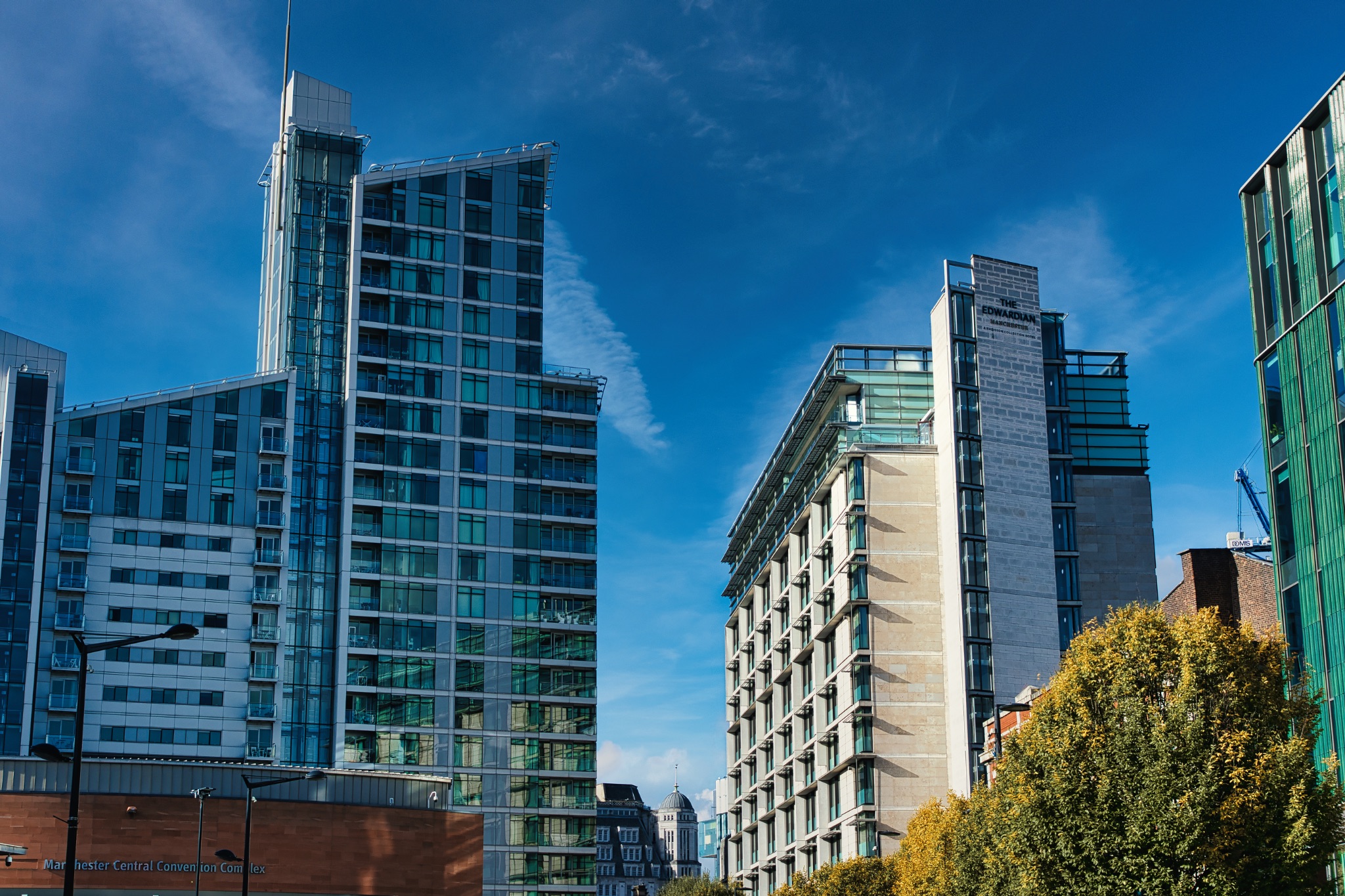 Tall Buildings with Glass and Stone Facades Against Blue Sky in Manchester, UK.